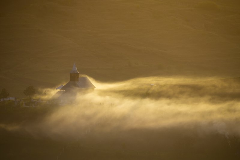 Wooden church on a hilltop, wrapped in waves of golden mist at sunrise. Sun rays piercing through the fog create a mystical atmosphere. Awarded photograph on 1x.com.